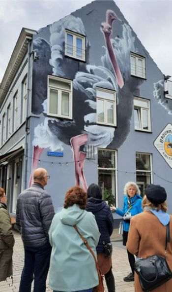 Gidsen met wandelaars bij een muurschildering van een struisvogel op een huis geschilderd.